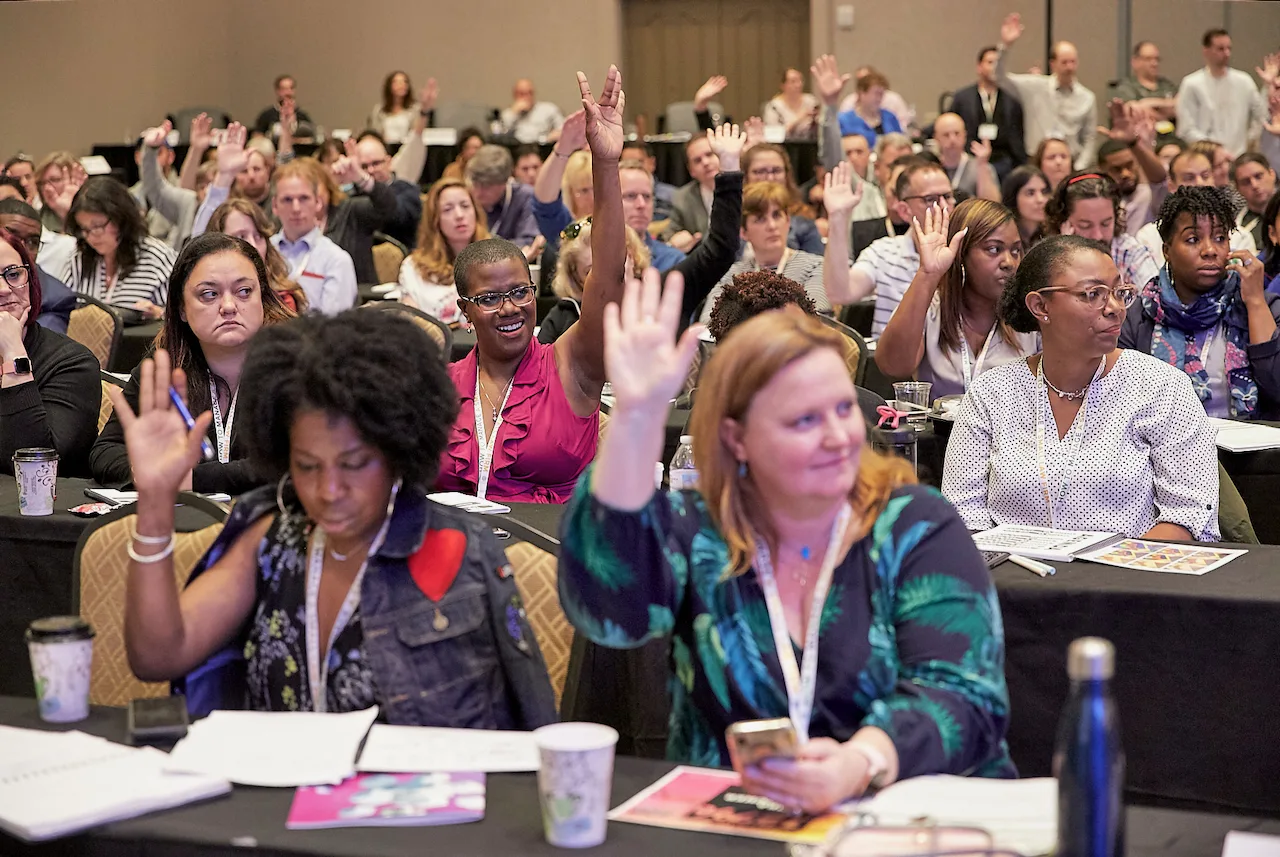 A full room of HTM members raising their hands during a live session.