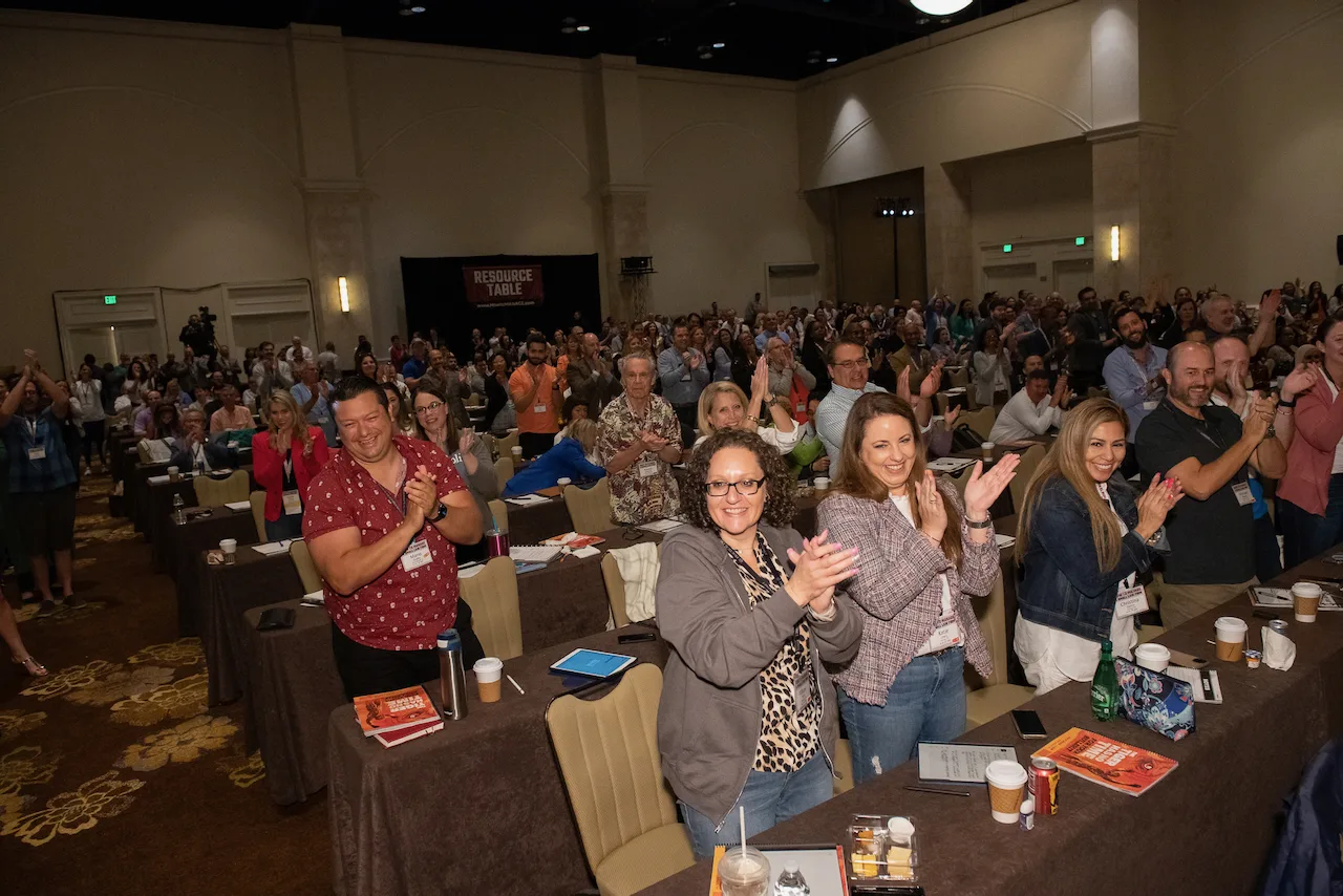 A large group of HTM members standing and applauding together in a ballroom.